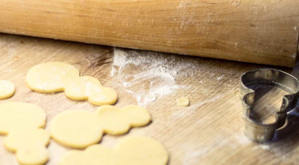 Cut out raw sugar cookies on a table next to a rolling pin