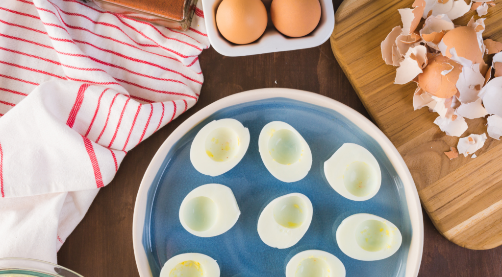 Hollowed out deviled eggs on a blue plate surrounded by egg shells and a red and white striped towel